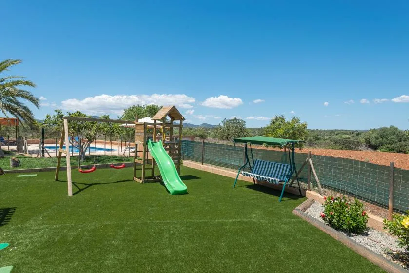 An outdoor play area with a green slide, swings, and a bench.