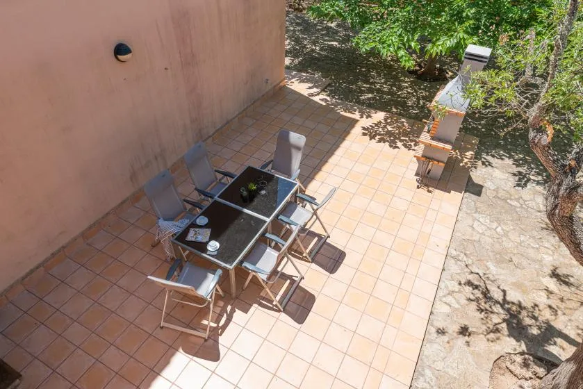 A tiled outdoor patio has a dining table and chairs beside a shaded garden.