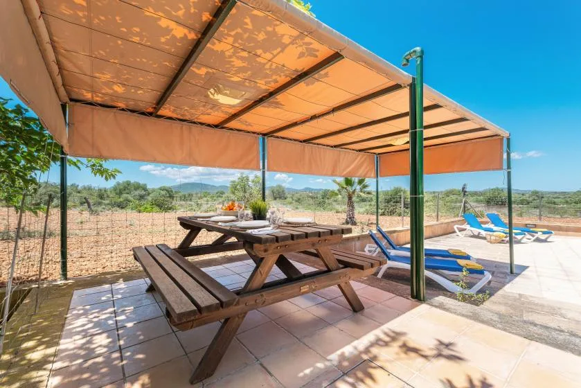 A shaded outdoor patio with picnic tables and lounge chairs beside a dry landscape.