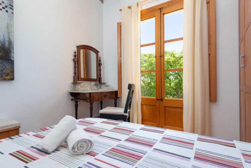 A bedroom with a striped bedspread, a dressing table, and glass doors opening to greenery.