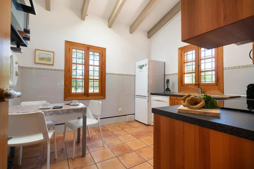 A bright kitchen and dining area with wooden-framed windows and a tiled floor.
