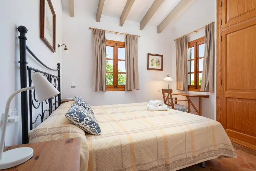 A bedroom with a neatly made bed and two curtained windows.