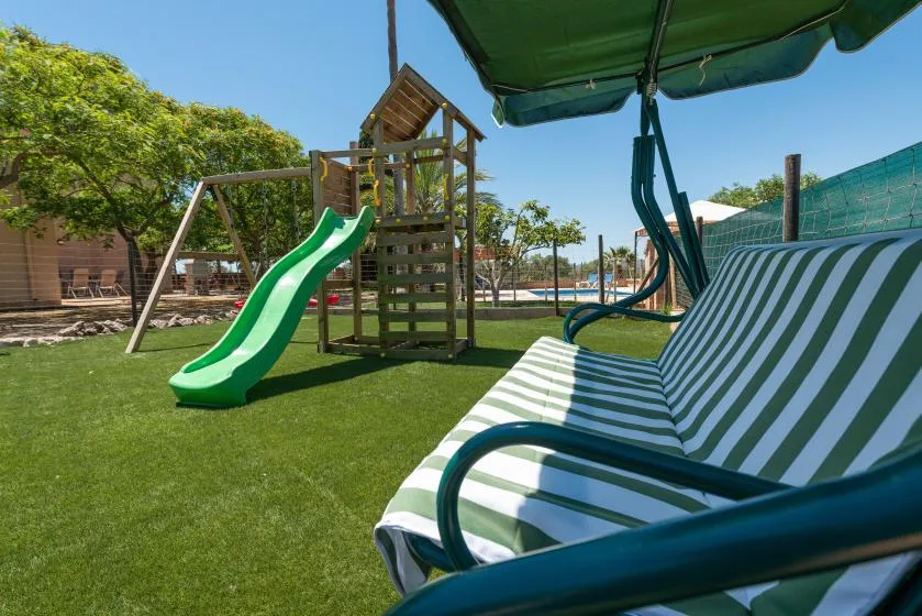 An outdoor play area with a green slide and striped seating beneath a shade umbrella.
