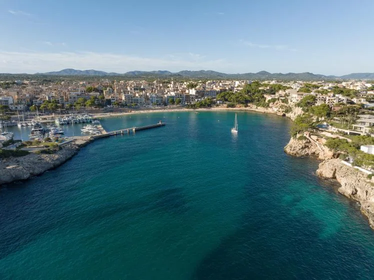 Aerial view of a coastal bay with turquoise water, rocky shores, and buildings along the coast.