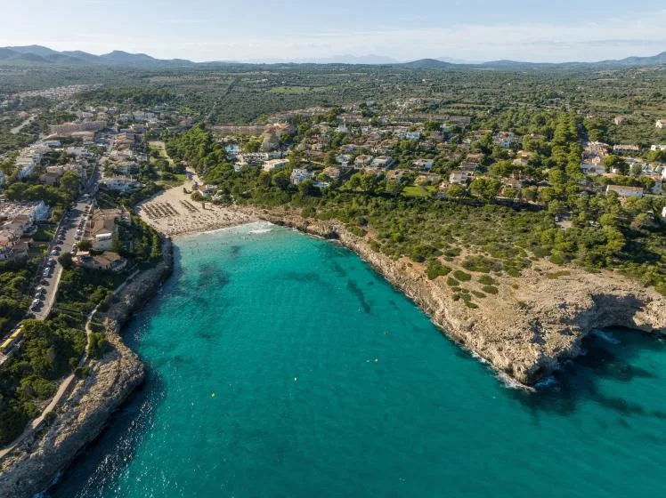 An aerial view shows a turquoise cove beside a sandy beach and coastal town.