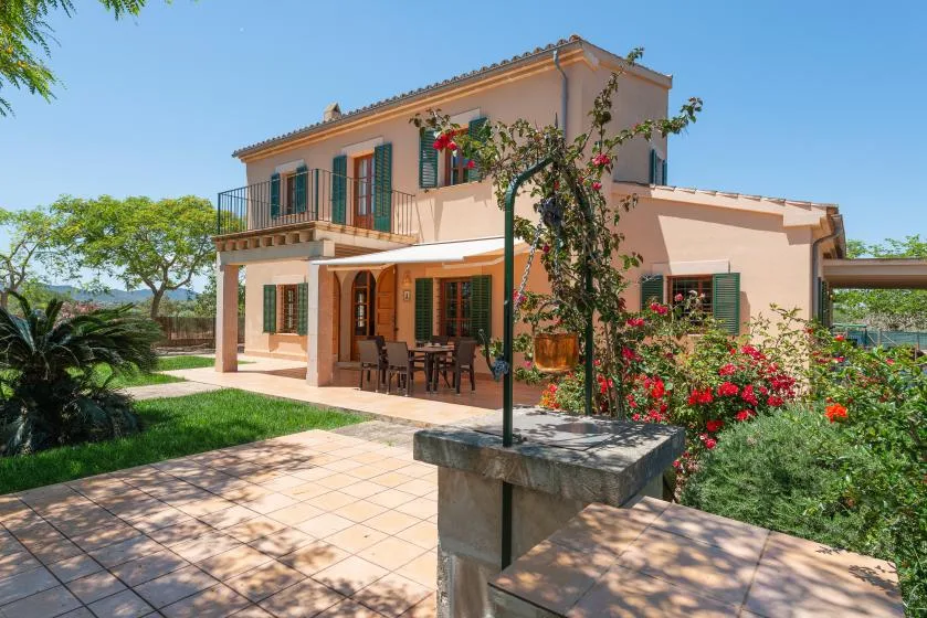 A peach-colored house opens onto a paved patio surrounded by flowering plants.