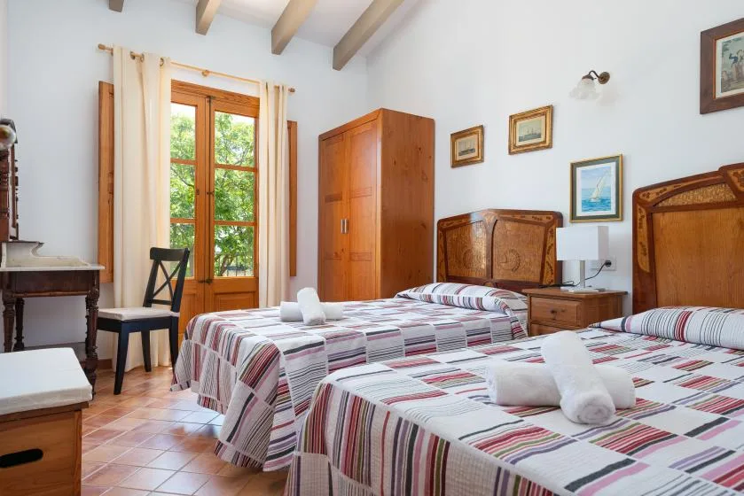 A bedroom with two beds, a wooden wardrobe, and a window overlooking greenery.