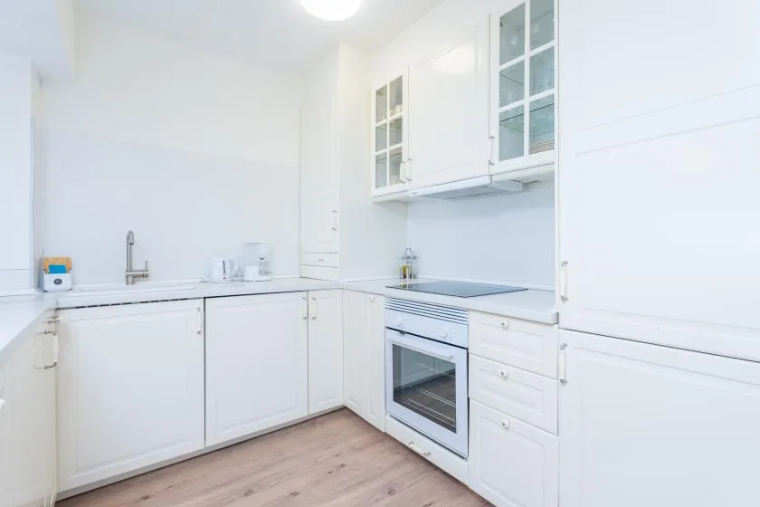 Una cocina blanca y luminosa con armarios, una placa de cocina y un horno.