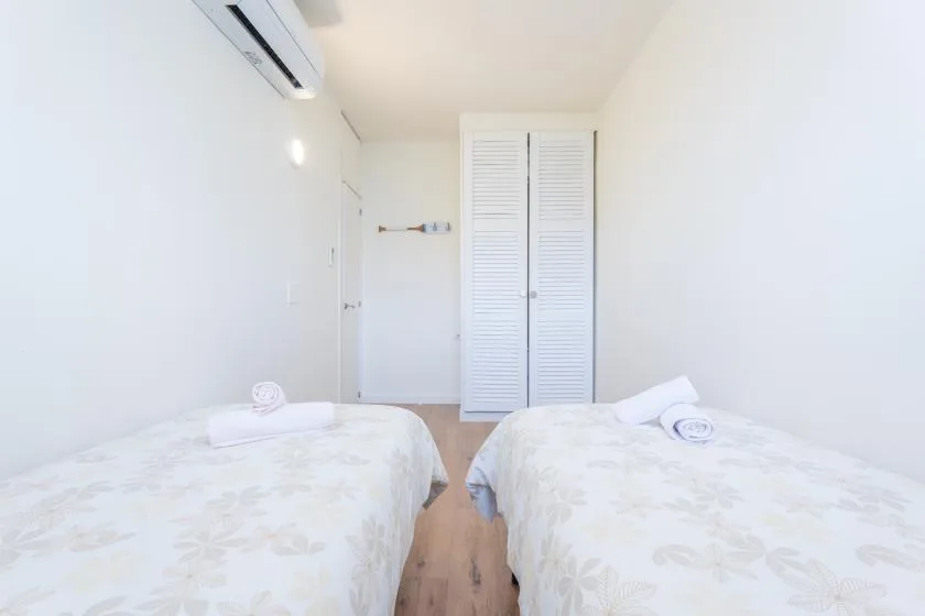 Un dormitorio luminoso con dos camas y un armario blanco de persianas.