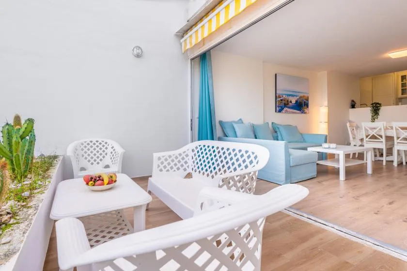 Un patio amueblado se abre a una sala de estar con asientos azules y muebles blancos de exterior.