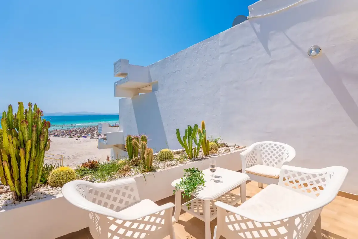 Un patio soleado tiene asientos blancos y vistas al mar.