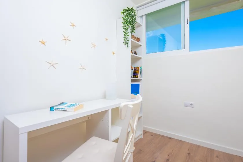Una luminosa zona de estudio con un escritorio blanco y una silla junto a una ventana.