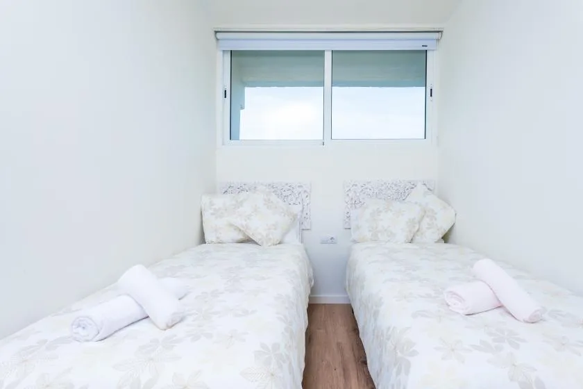 Un dormitorio luminoso con dos camas bajo una ventana.