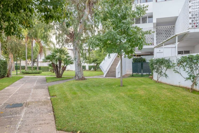 Un patio ajardinado con un sendero pavimentado, césped, árboles y una escalera exterior.