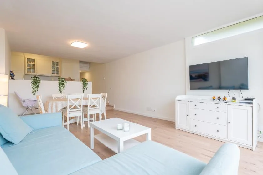 Una luminosa sala de estar y comedor con asientos, una mesa de comedor y un televisor en la pared.