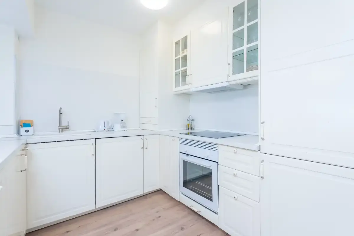 Una cocina blanca y luminosa con armarios, fregadero y horno.