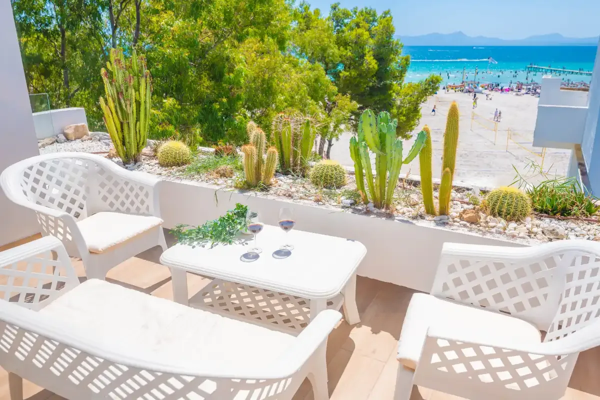 Un patio junto al mar con asientos blancos da a una playa de arena y al mar.