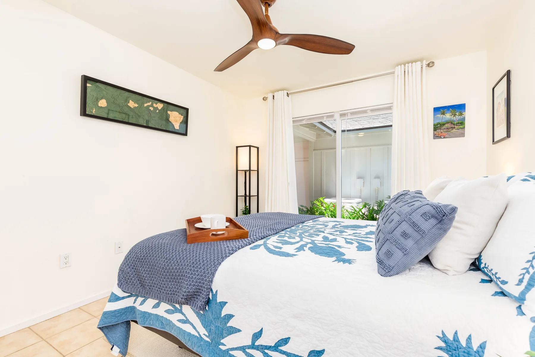 Un dormitorio con una cama vestida de blanco y azul junto a puertas de vidrio con cortinas.
