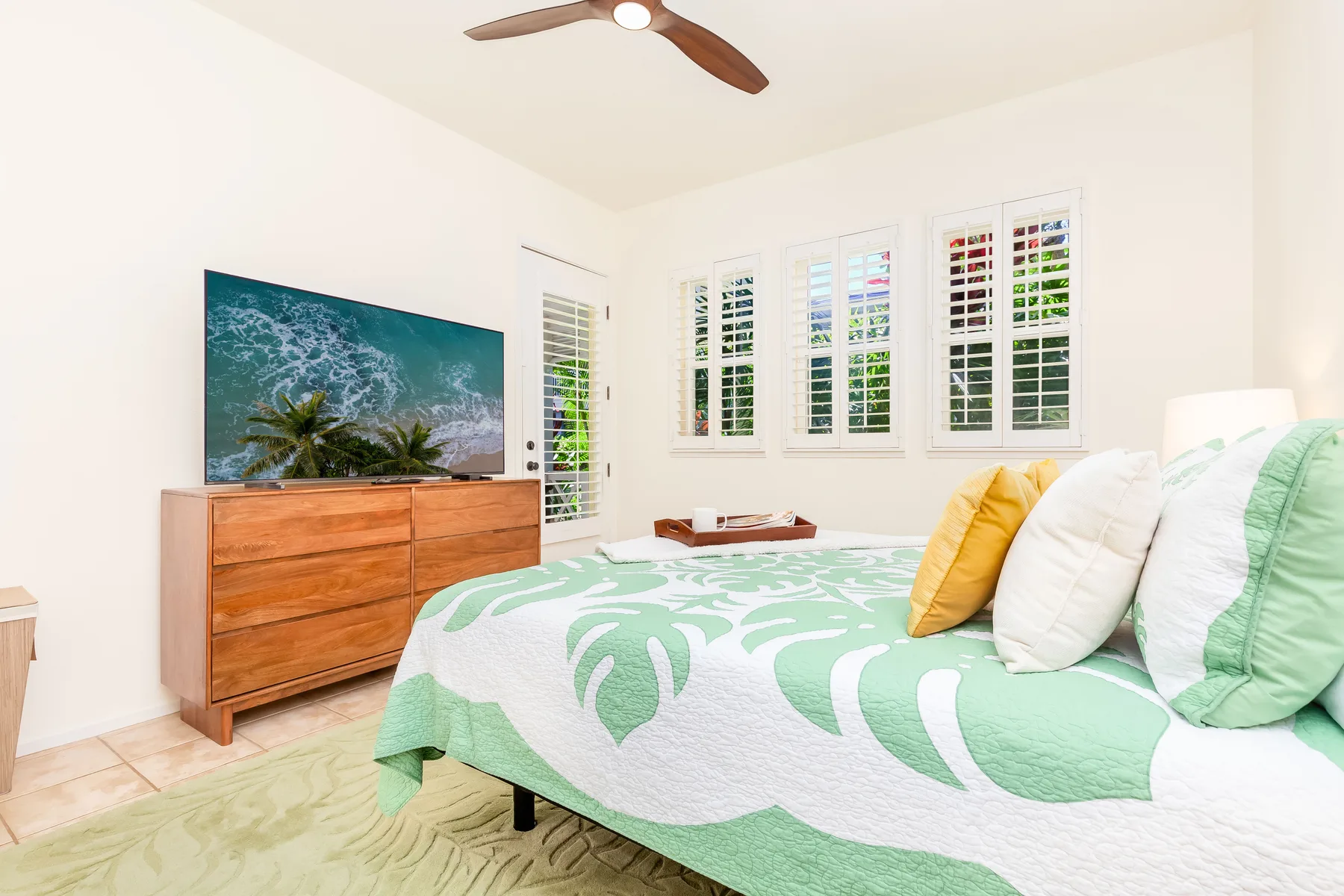 Un dormitorio luminoso tiene una cama con ropa de cama verde estampada con hojas y una cómoda de madera.