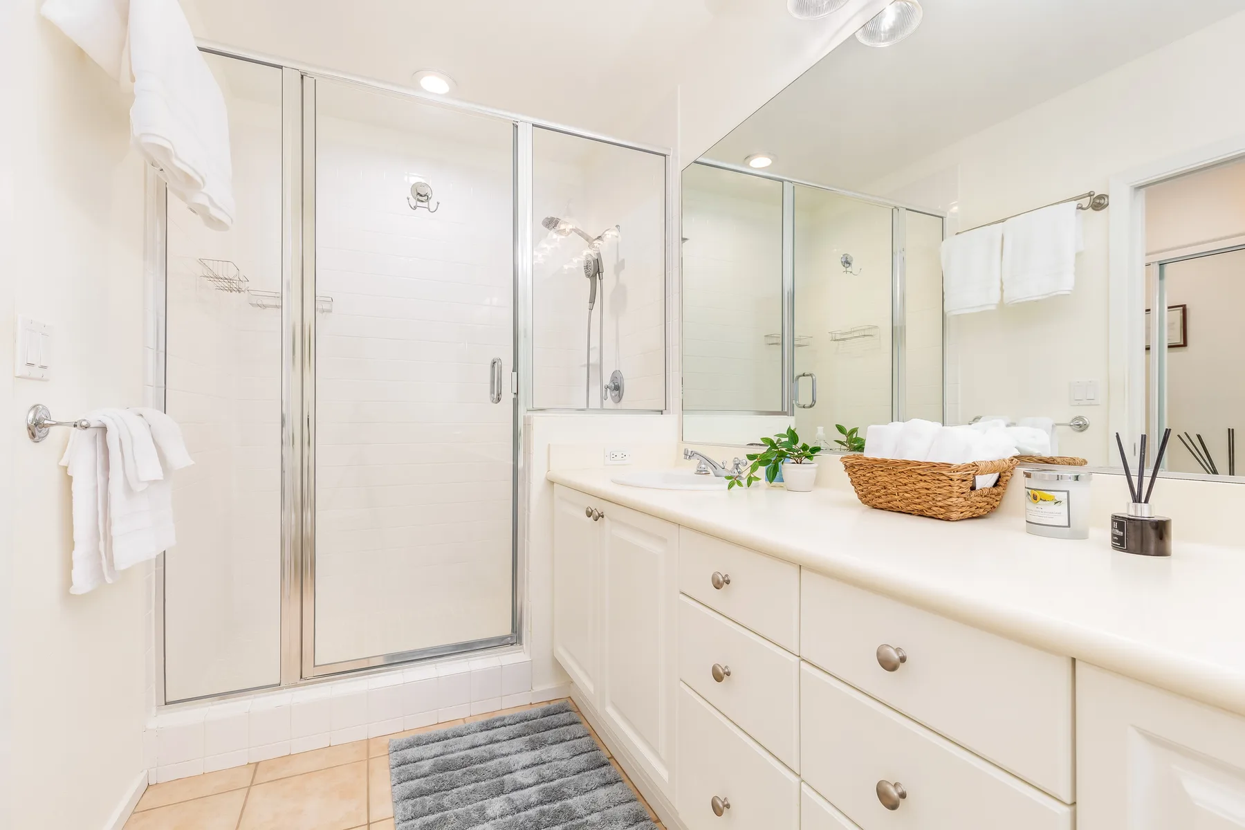 Un baño luminoso con una ducha de vidrio y un tocador largo.