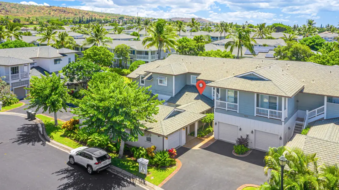 Vista aérea de un vecindario residencial con casas, palmeras y una calle.
