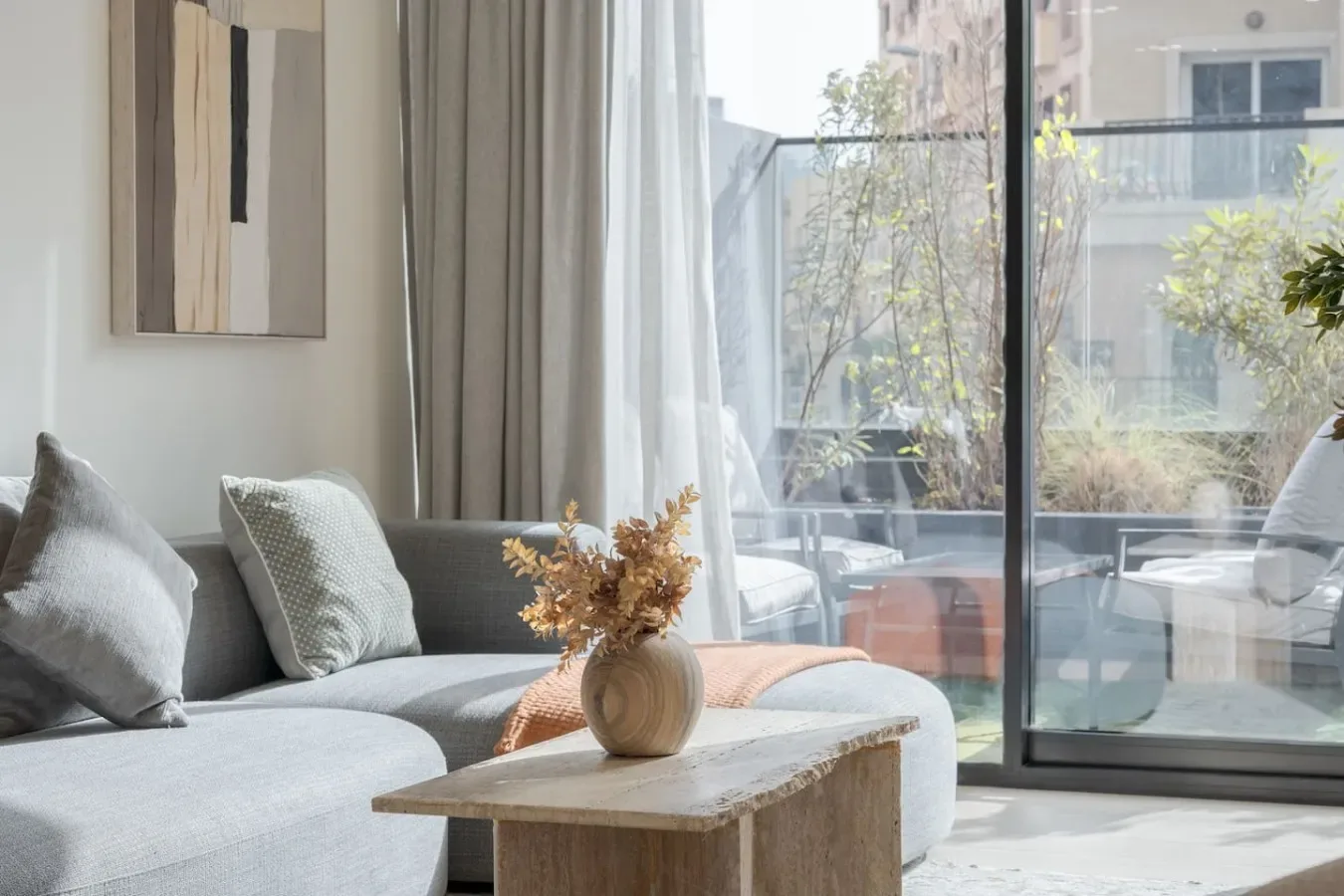 A bright living room has a gray seating area beside large windows overlooking a patio.