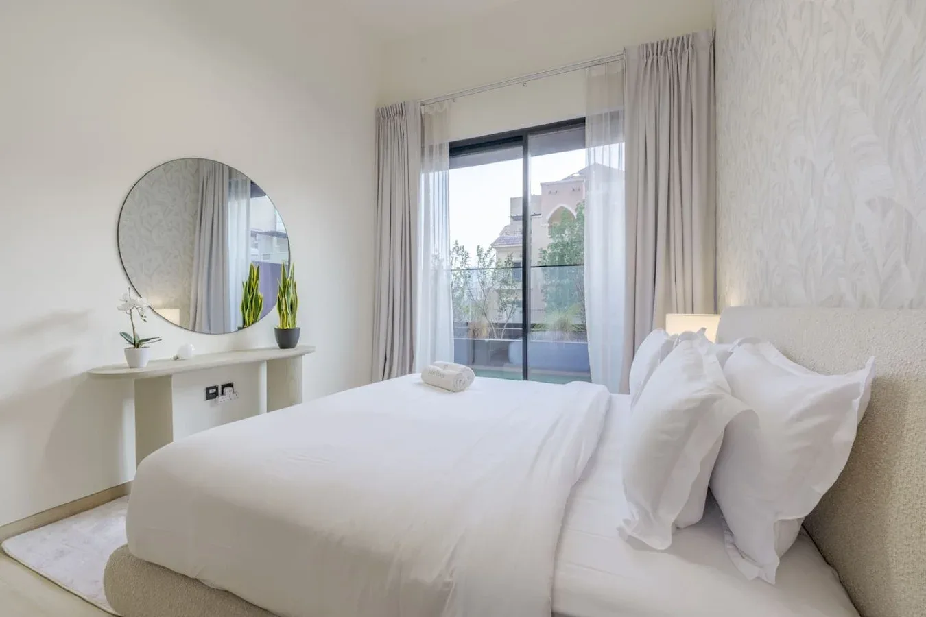 A bright bedroom with white bedding and a glass door opening to a balcony.
