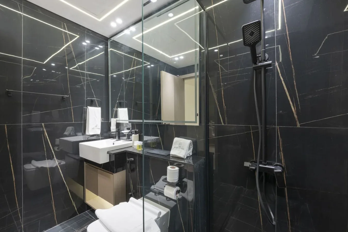 A modern bathroom with a glass shower, dark tiled walls, and a sink.