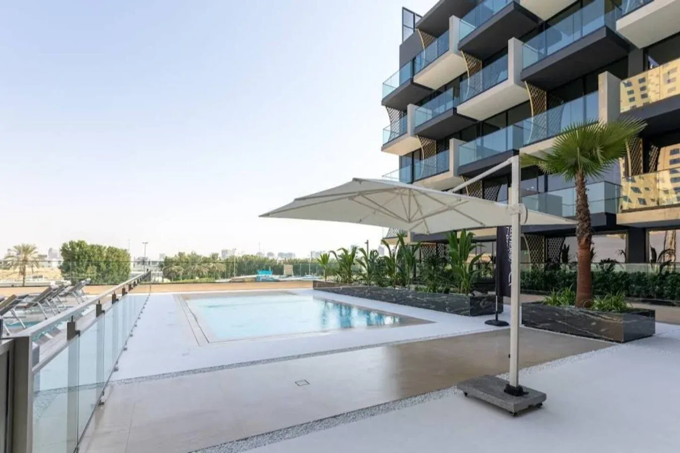 An outdoor swimming pool sits beside a modern building with balconies.
