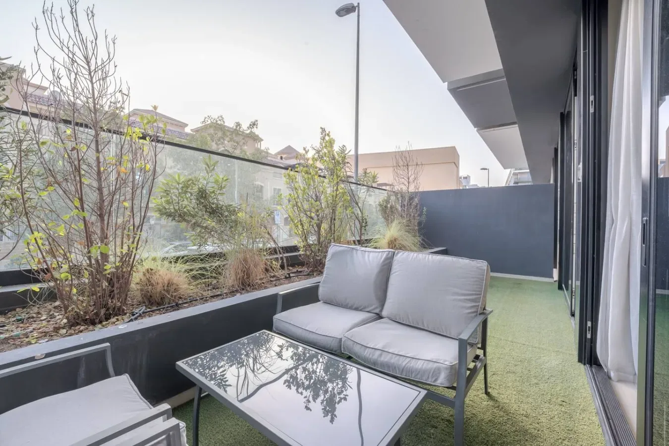 A small outdoor seating area with a cushioned sofa and low table beside glass doors.