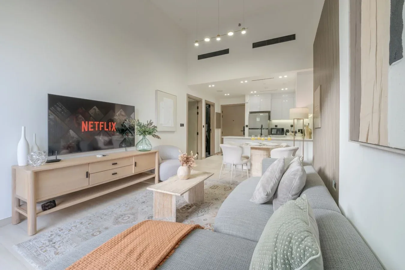 A bright living room opens into a kitchen and dining area, with a television and seating.
