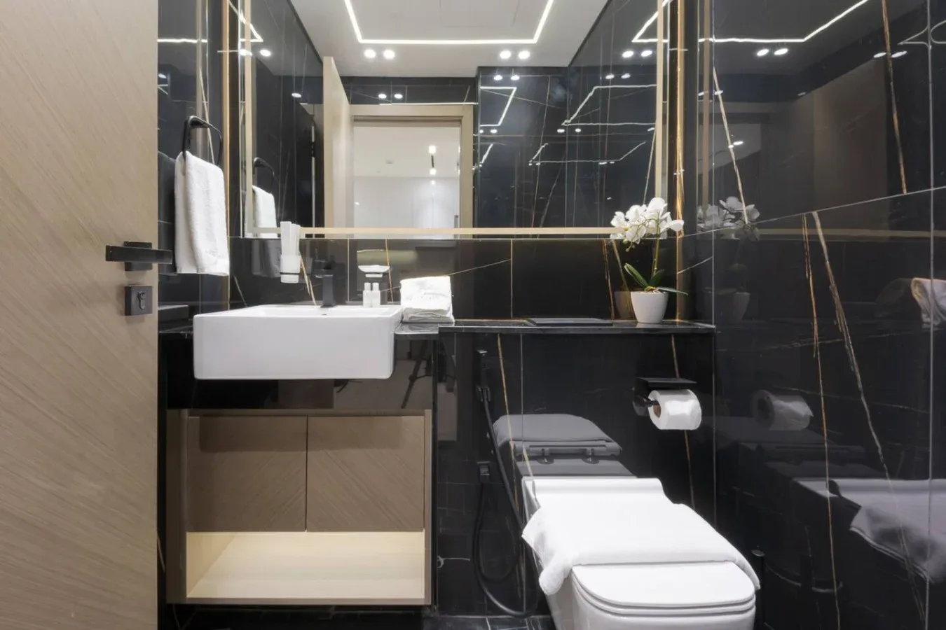 A modern bathroom with a sink, toilet, and dark reflective wall panels.