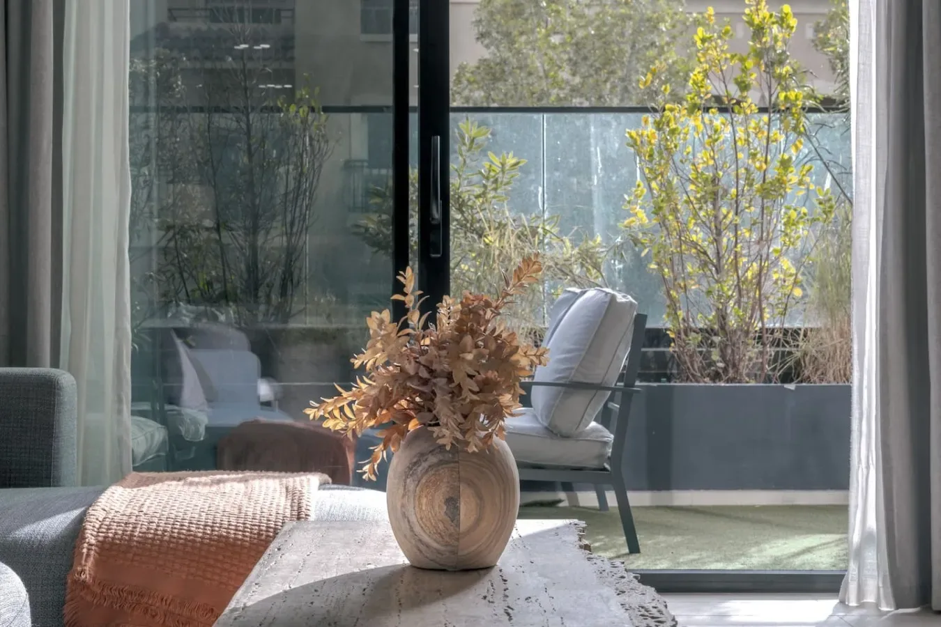 A seating area beside large glass doors, with a vase of dried flowers on the table.