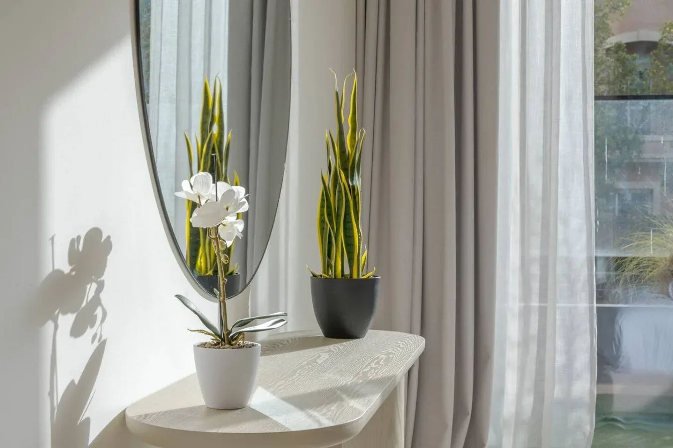 A sunlit corner with a small table, potted plants, and curtains beside a window.