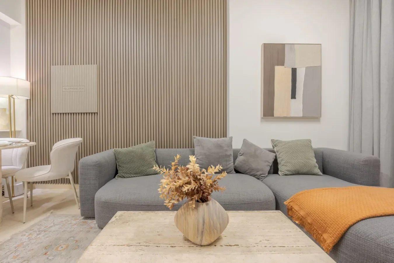A modern living room with gray seating, neutral artwork, and a vase of dried flowers.