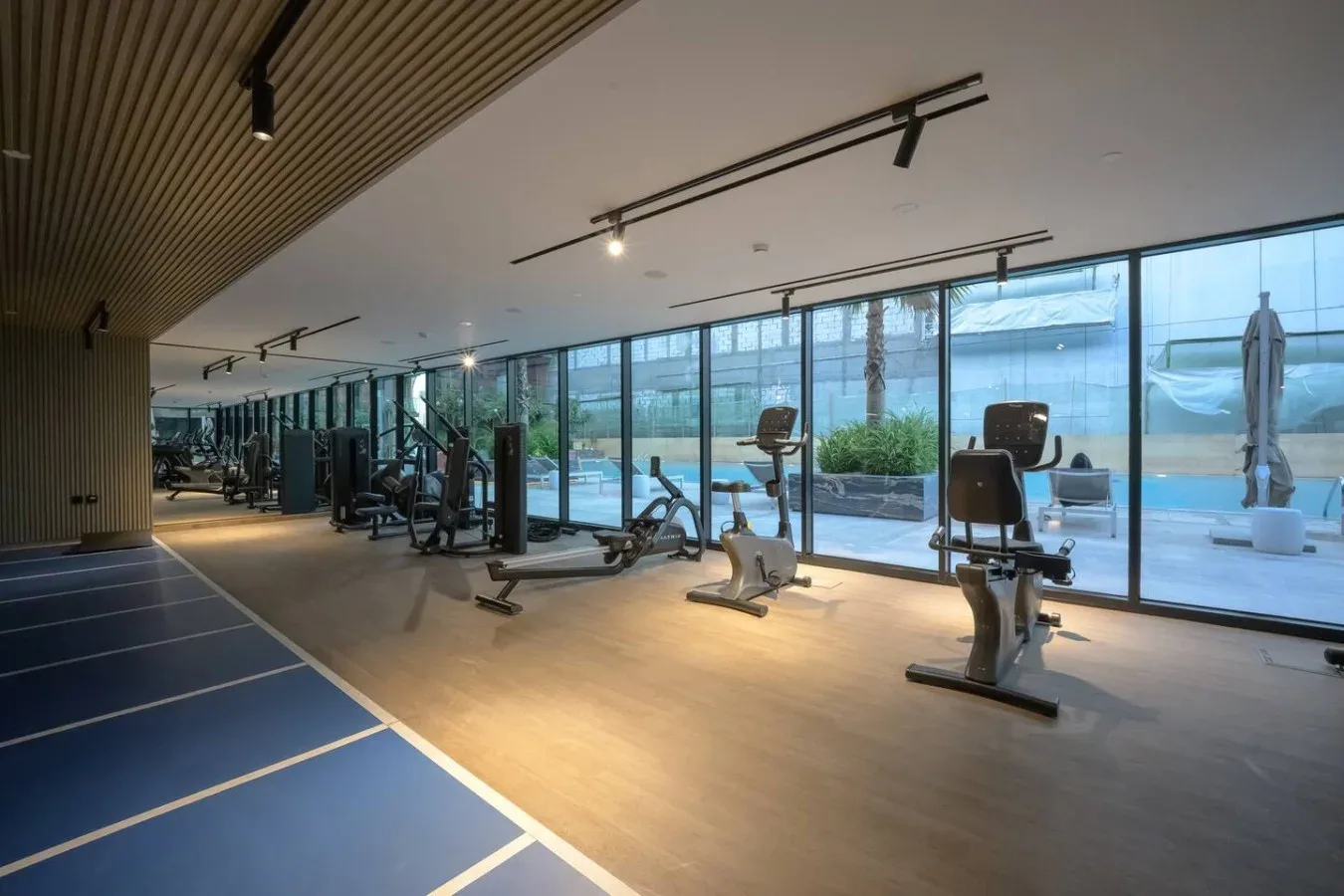 A gym with exercise machines beside floor-to-ceiling windows.