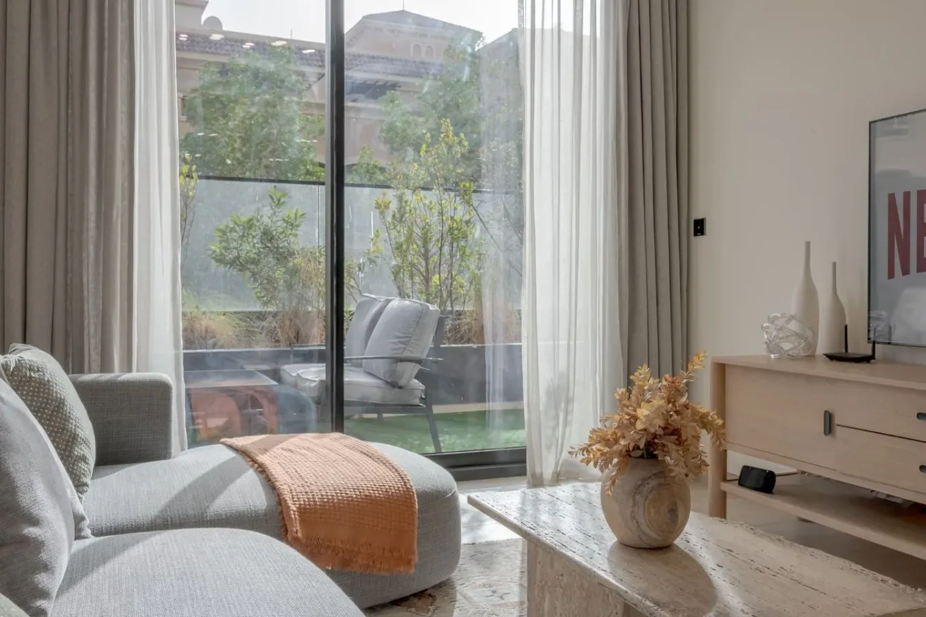A bright living room with seating beside a large window overlooking greenery.