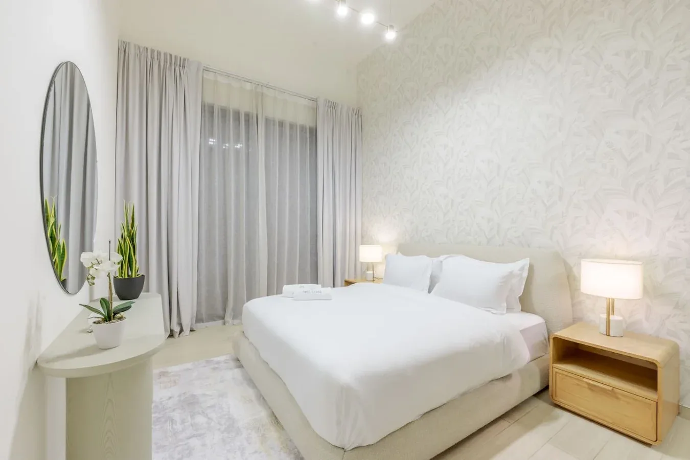 A bright bedroom with a neatly made bed and curtains across the window.