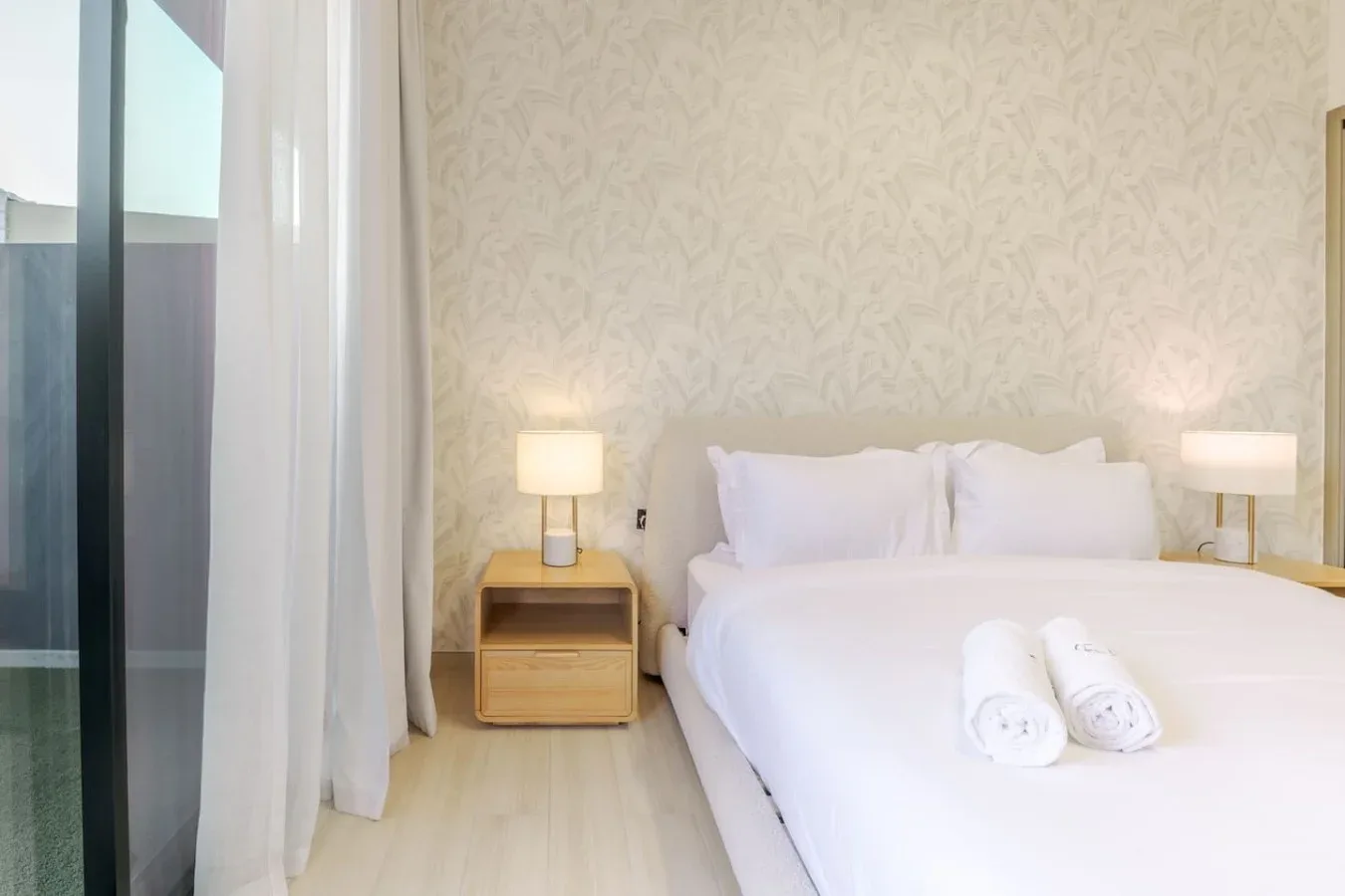 A bright bedroom features a neatly made bed and matching bedside lamps.