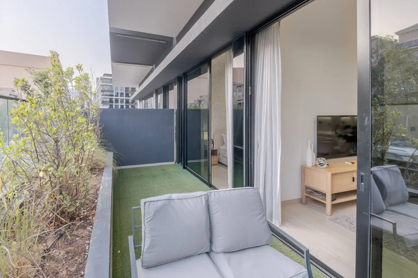 A furnished patio with seating faces glass doors and a planted garden.