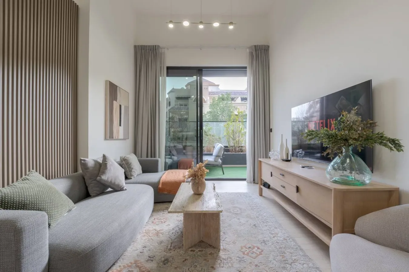 A living room with seating, a television, and glass doors opening onto a balcony.