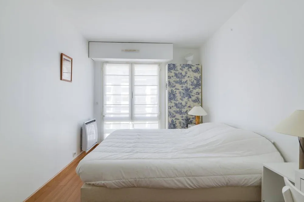 A bright bedroom with a neatly made bed and a large window.