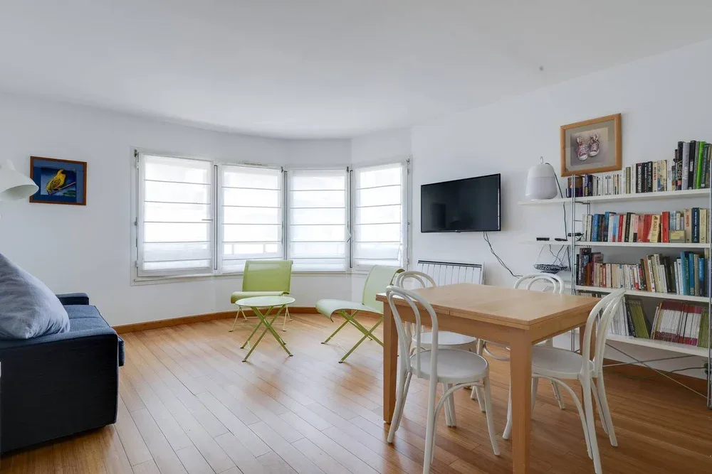 Un salón-comedor luminoso con grandes ventanas y una mesa de madera.