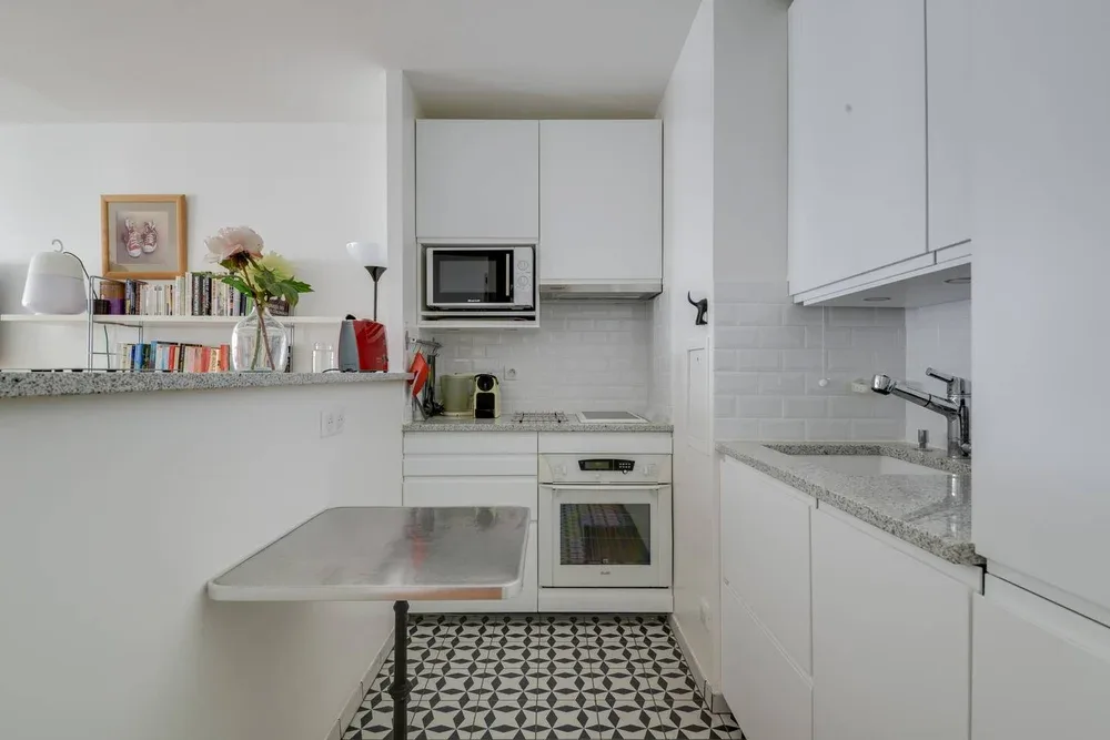 Una cocina compacta con gabinetes blancos, una encimera y un suelo estampado.