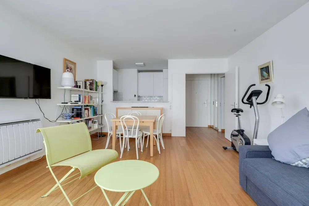 A bright living and dining area with a table, seating, and exercise equipment.
