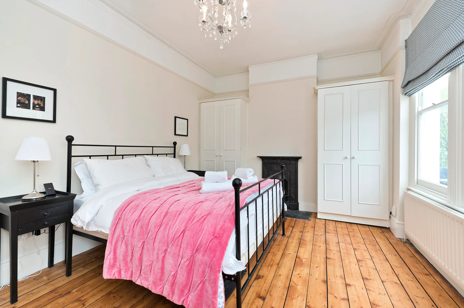 A bright bedroom with a black metal bed, white bedding, and a pink blanket.