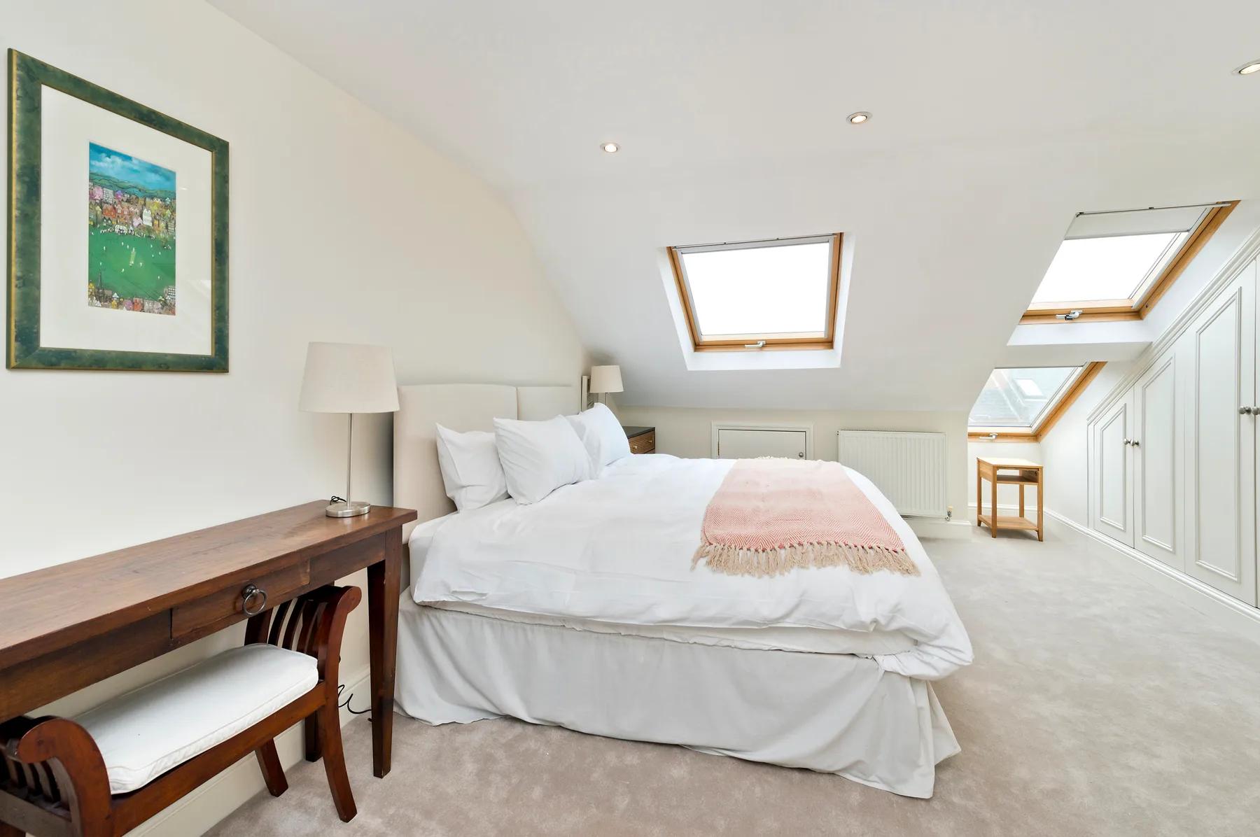 A bright bedroom with a bed, framed artwork, and sloped skylights.