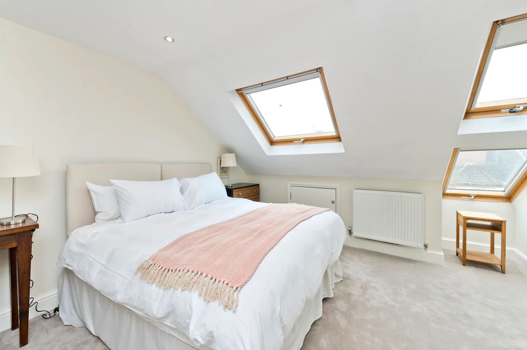 A bright attic bedroom with a bed beneath sloped ceilings and skylights.