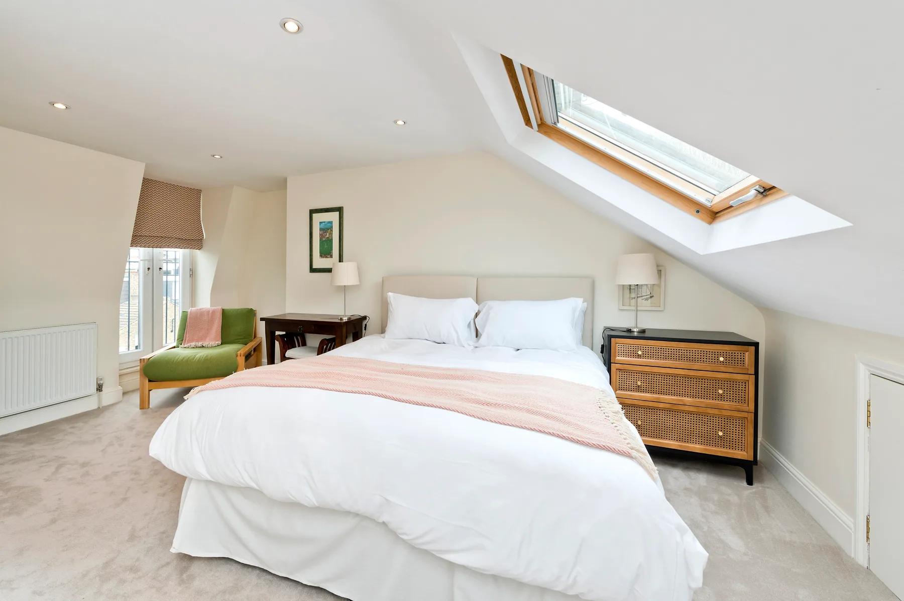 A bright bedroom with a bed beneath a sloped ceiling and skylight.
