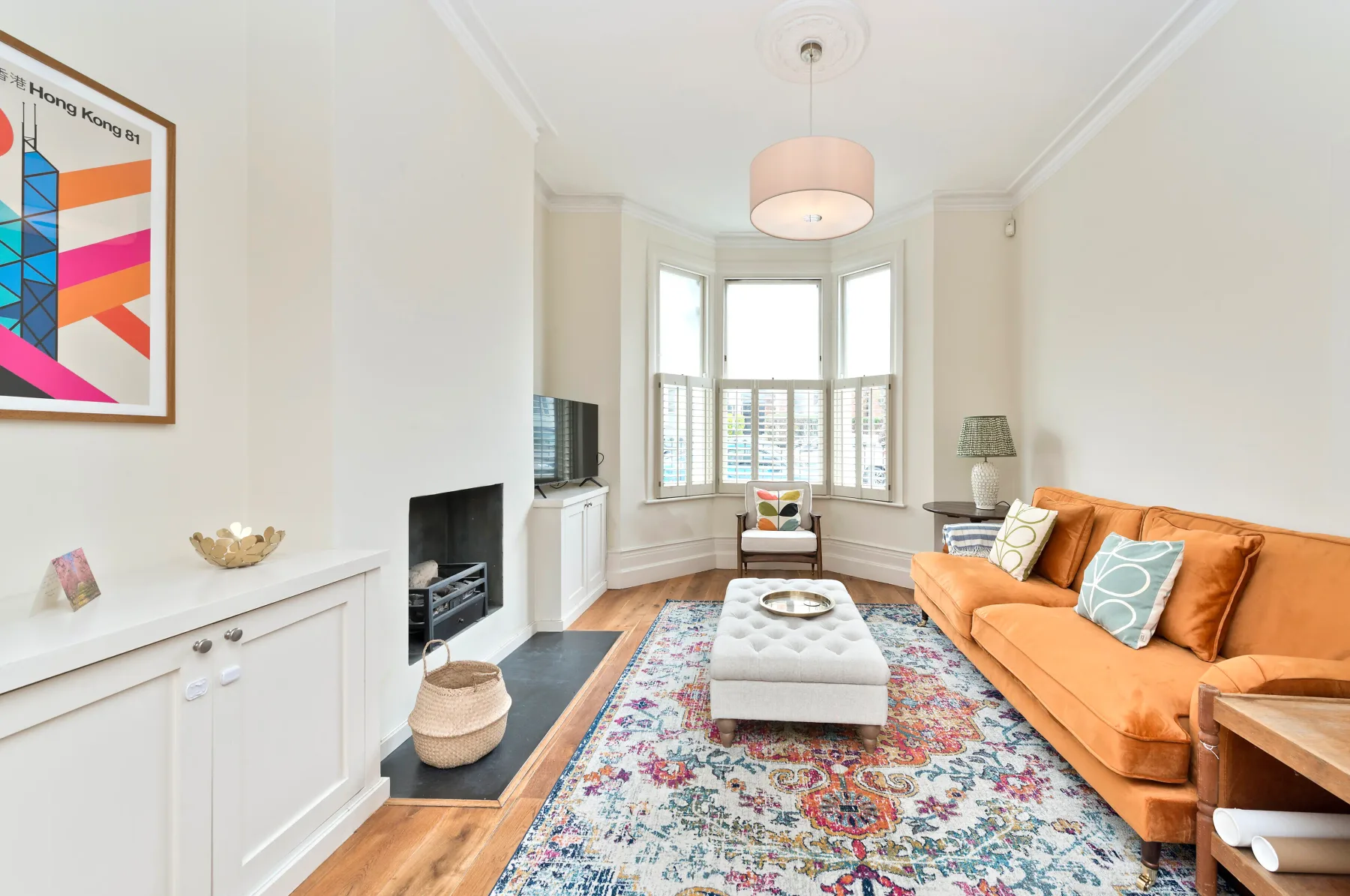 A bright living room with a bay window and orange seating.